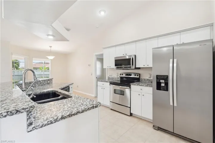 Kitchen featuring decorative light fixtures, light stone countertops, stainless steel appliances, sink, and lofted ceiling