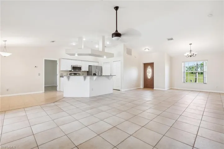 Unfurnished living room featuring ceiling fan with notable chandelier, lofted ceiling, and light tile patterned floors