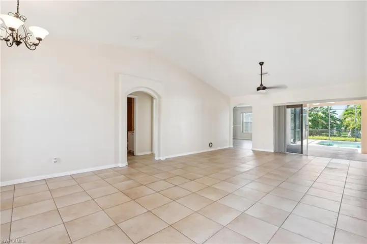 Tiled spare room featuring ceiling fan with notable chandelier and high vaulted ceiling