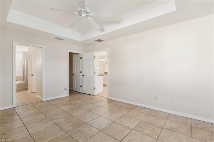 Unfurnished bedroom featuring a raised ceiling, ceiling fan, ornamental molding, and ensuite bathroom