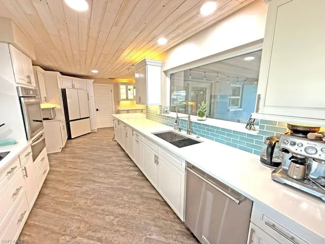Kitchen with stainless steel appliances, decorative backsplash, white cabinetry, light wood finished floors, and recessed lighting