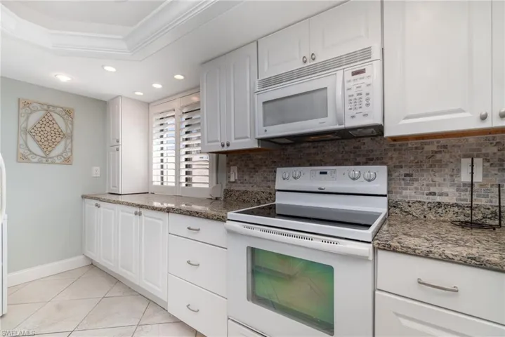 Kitchen featuring white appliances, tiled backsplash, white cabinetry, recessed lighting, and granite countertops.