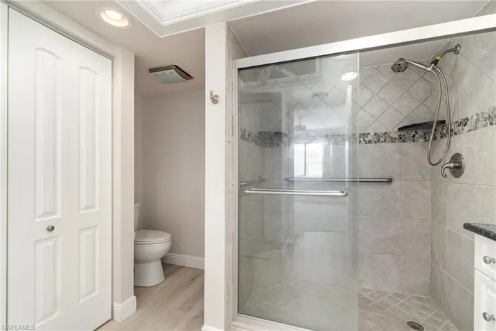 Full bath featuring a shower stall, toilet, wood finished floors, baseboards, and recessed lighting
