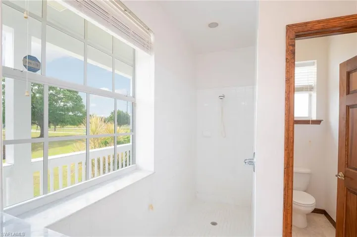 Bathroom with healthy amount of natural light, toilet, tiled shower, and tile patterned flooring