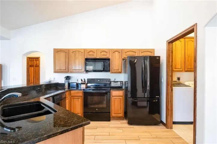 Kitchen with black appliances, a sink, independent washer and dryer, arched walkways