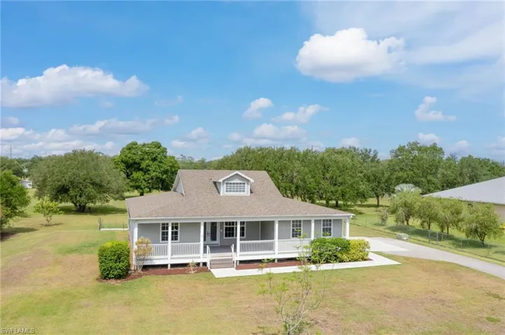 Farmhouse-style home featuring covered porch, a front yard, a shingled roof, and concrete driveway
