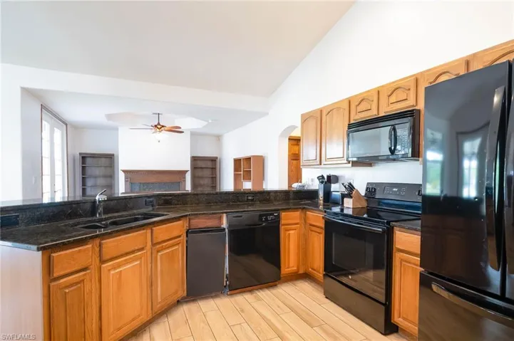 Kitchen with black appliances, a sink, arched walkways, dark stone countertops, and a ceiling fan