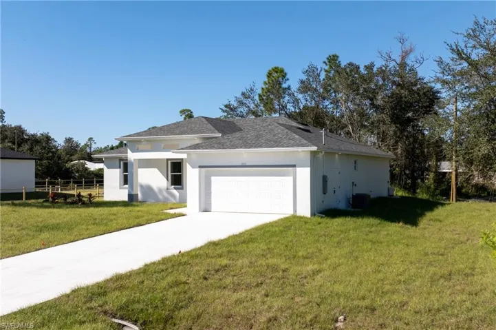 View of side of home with concrete driveway, stucco siding, a garage, and roof with shingles