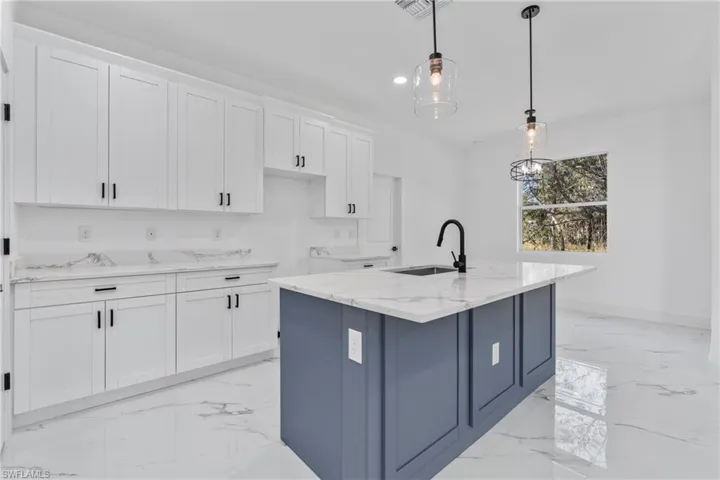Kitchen with light stone counters, white cabinets, decorative light fixtures, recessed lighting, and a center island with sink