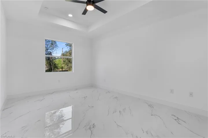 Empty room with marble finish floors, a raised ceiling, recessed lighting, and a ceiling fan