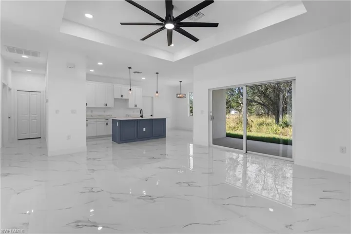 Unfurnished living room with a raised ceiling, light marble finish floors, recessed lighting, and a ceiling fan