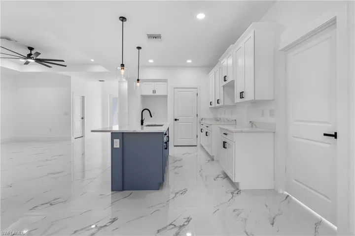 Kitchen featuring white cabinetry, a center island with sink, hanging light fixtures, open floor plan, and light stone countertops