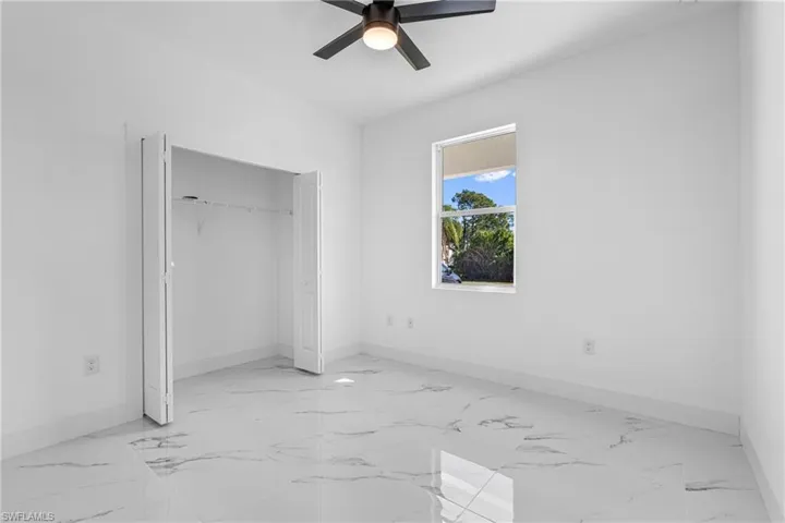 Unfurnished bedroom with light marble finish floors, a closet, and ceiling fan