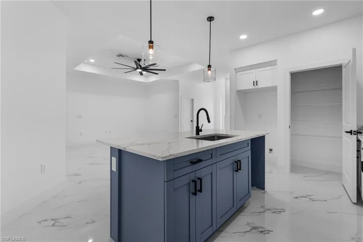 Kitchen featuring blue cabinetry, white cabinetry, light stone counters, recessed lighting, and decorative light fixtures