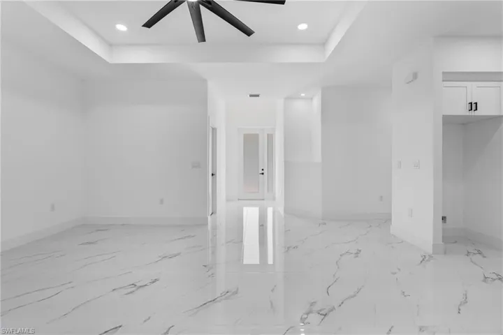Unfurnished room with a tray ceiling, recessed lighting, light marble finish floors, and ceiling fan