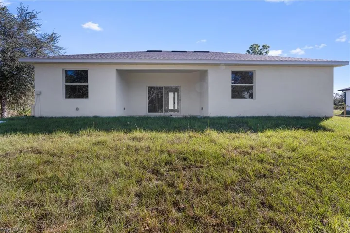 Back of house with stucco siding, a lawn, and a patio area