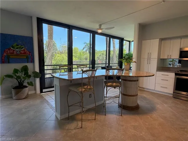 Kitchen featuring a granite-topped island with seating, a granite-topped round breakfast bar, tile flooring, white cabinetry, and stainless steel appliances