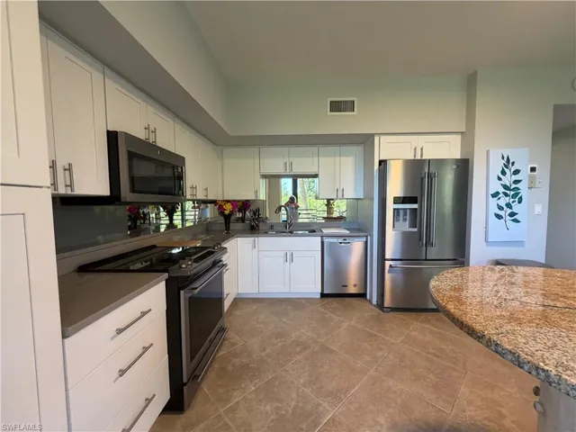 Kitchen featuring white shaker-style cabinetry, stainless steel appliances, a mirrored backsplash, and a granite-topped peninsula