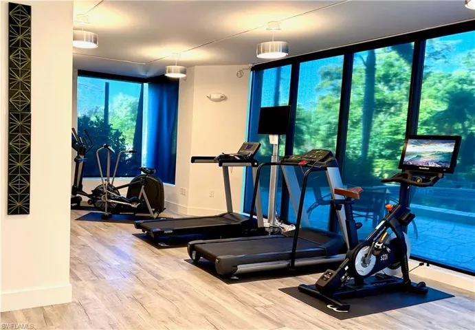 Fitness room featuring wood-finish flooring, recessed lighting, and expansive windows with roller shades