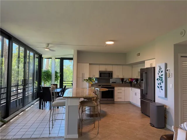 Open-concept kitchen featuring an island with granite-finish countertop, light-toned cabinetry, stainless steel appliances, and tile flooring