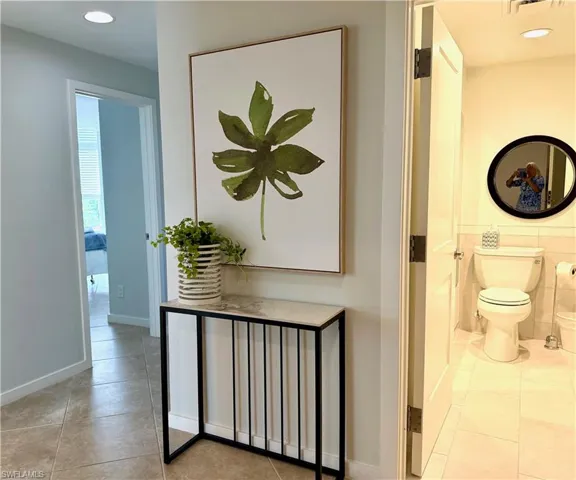 Hallway featuring tile flooring and a doorway leading to a room with window blinds