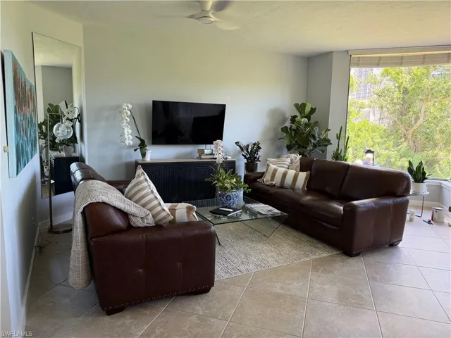 Spacious living area featuring large windows, neutral-toned tile flooring, and a ceiling fan