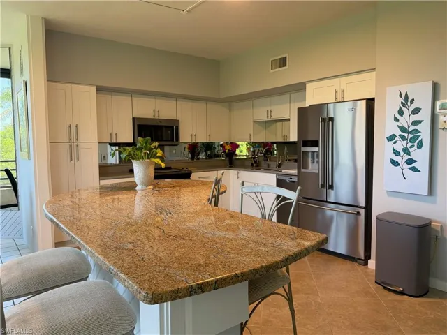 Kitchen featuring an island with a polished stone countertop, white cabinetry with silver hardware, stainless steel appliances, a mirrored backsplash, and tile flooring