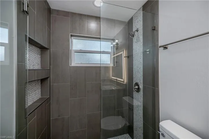 Bathroom with a healthy amount of sunlight, tiled shower, and toilet