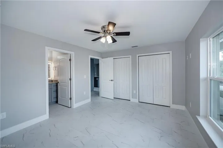 Unfurnished bedroom with two closets, ensuite bathroom, ceiling fan, and light tile floors