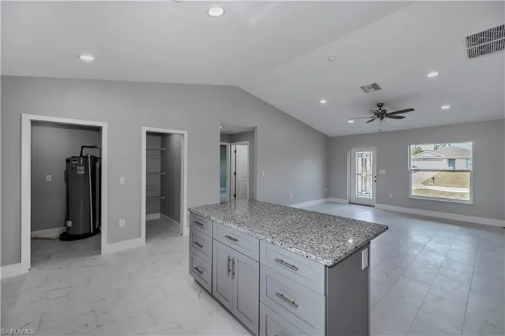 Kitchen with ceiling fan, vaulted ceiling, light tile flooring, and water heater