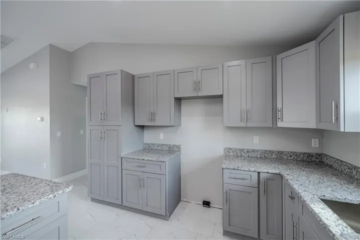 Kitchen featuring light stone counters, gray cabinets, light tile flooring, and lofted ceiling