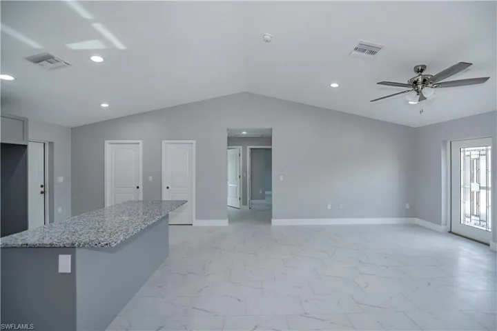 Kitchen with light stone countertops, ceiling fan, light tile floors, and lofted ceiling