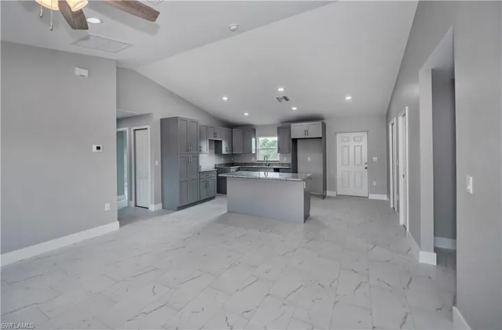 Kitchen featuring a center island, light tile floors, stone counters, ceiling fan, and vaulted ceiling