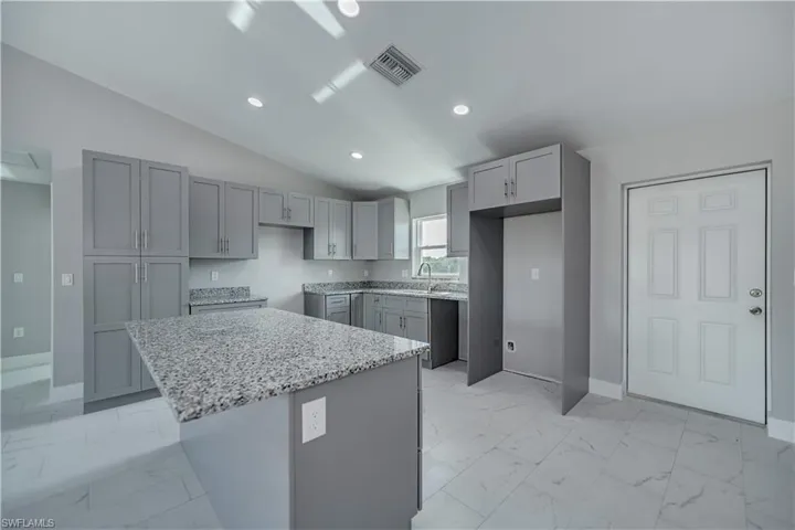 Kitchen with a center island, lofted ceiling, light tile floors, and gray cabinets