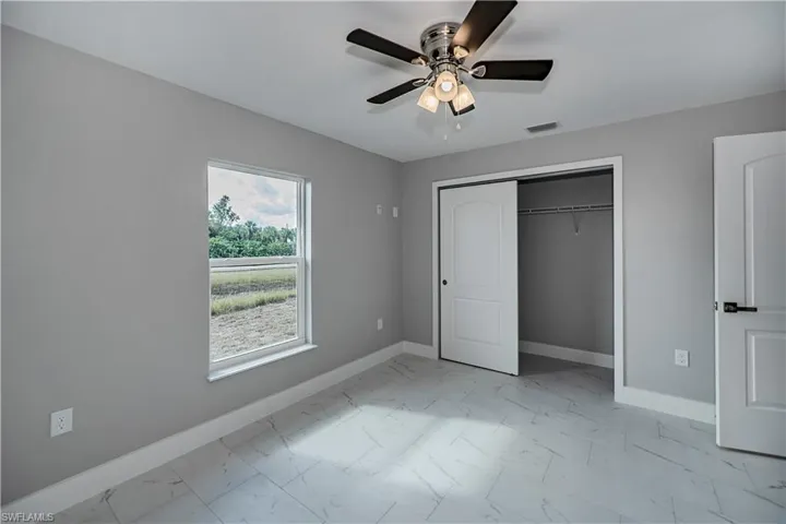 Unfurnished bedroom with a closet, ceiling fan, light tile flooring, and multiple windows