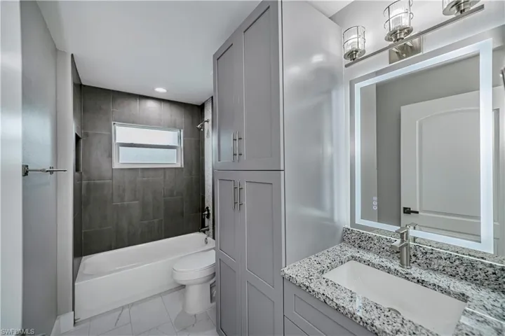 Full bathroom with tile flooring, toilet, large vanity, and tiled shower / bath