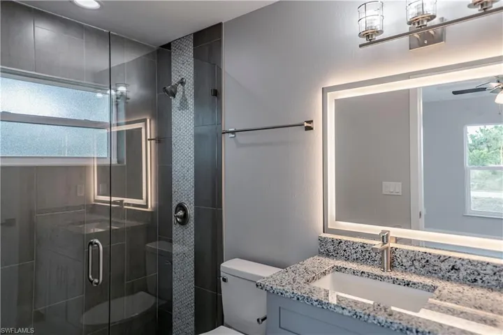 Bathroom with an enclosed shower, toilet, ceiling fan, and vanity