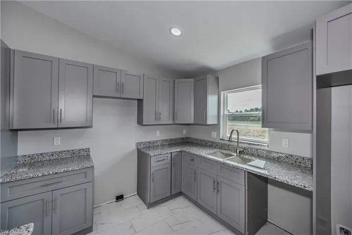 Kitchen featuring vaulted ceiling, light stone counters, light tile floors, gray cabinetry, and sink
