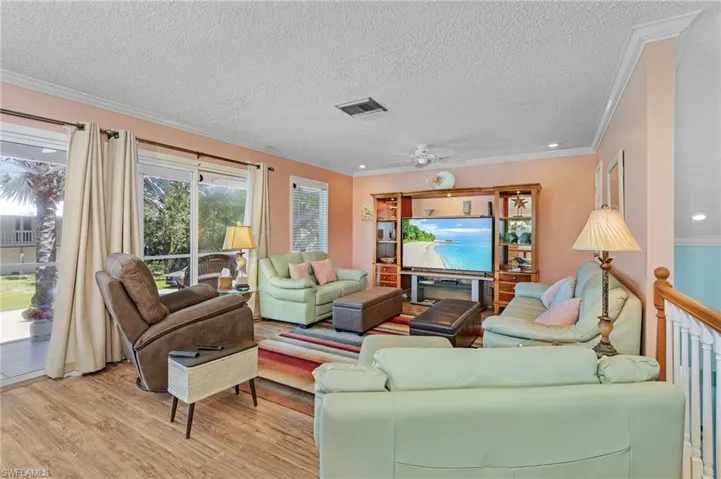 Living room with ceiling fan, a textured ceiling, ornamental molding, and light hardwood / wood-style floors