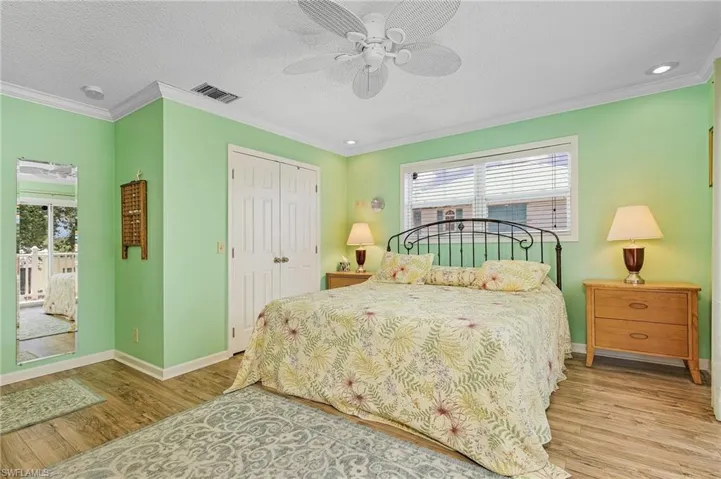 Bedroom featuring ceiling fan, light wood-type flooring, multiple windows, and ornamental molding