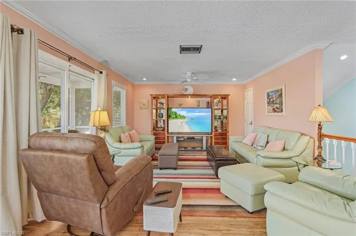 Living room featuring light wood-type flooring, ornamental molding, and a textured ceiling