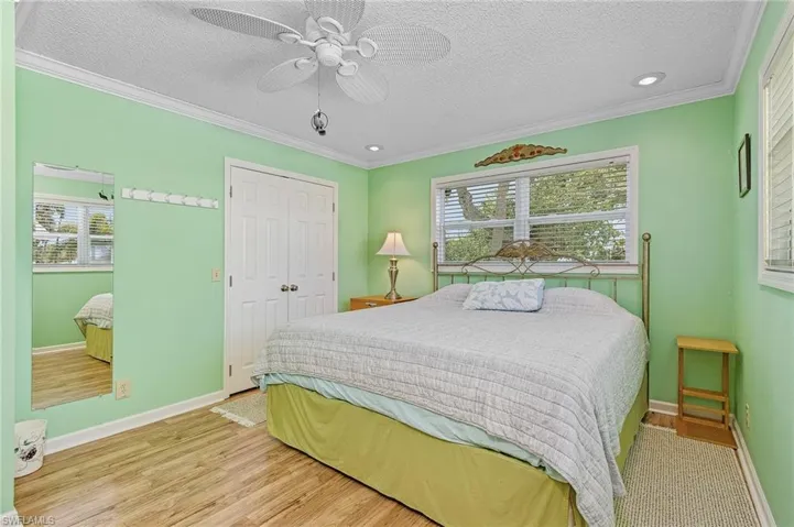 Bedroom featuring light wood-type flooring, a textured ceiling, crown molding, a closet, and ceiling fan