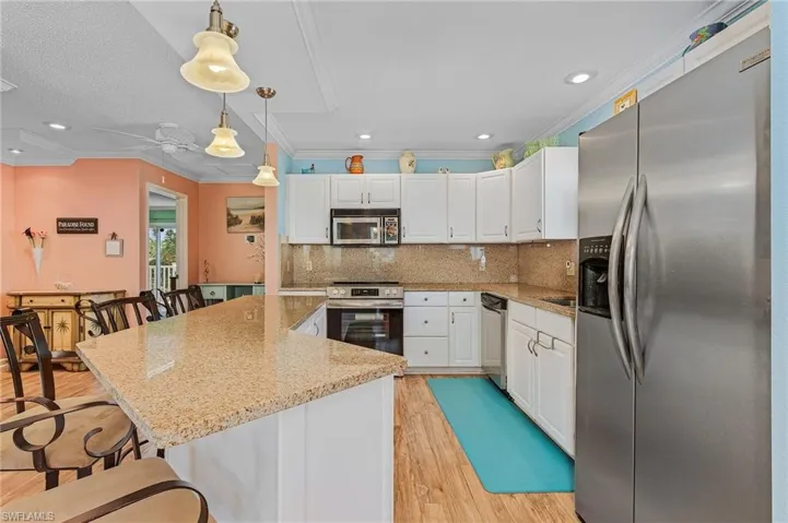 Kitchen with light stone countertops, stainless steel appliances, a kitchen breakfast bar, and light hardwood / wood-style floors