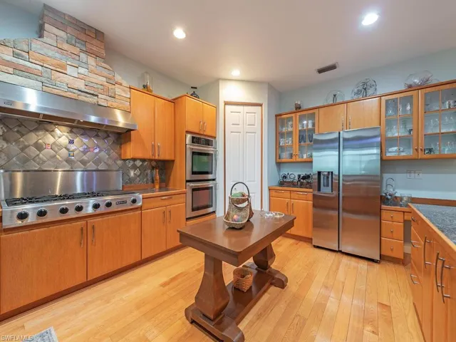 Kitchen featuring appliances with stainless steel finishes, light wood finished floors, tasteful backsplash, glass insert cabinets, and recessed lighting