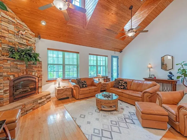Living area with ceiling fan, hardwood / wood-style floors, high vaulted ceiling, wood ceiling, and a stone fireplace