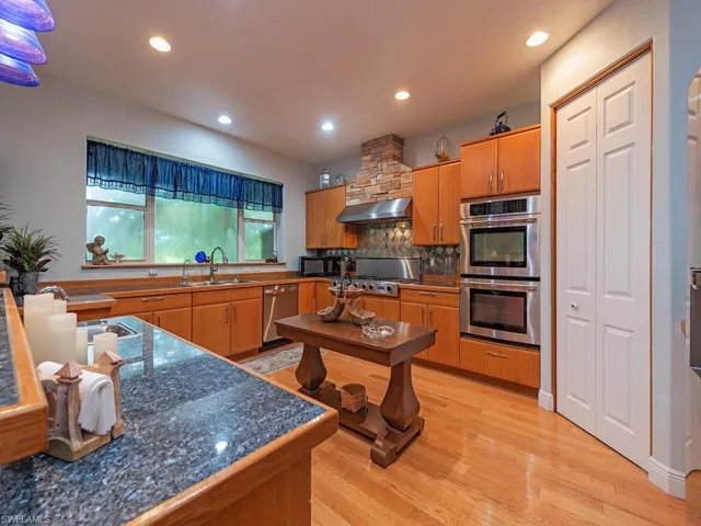 Kitchen with appliances with stainless steel finishes, range hood, decorative backsplash, light wood finished floors, and recessed lighting