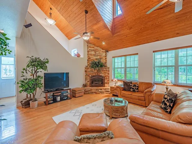Living room with ceiling fan, high vaulted ceiling, wood finished floors, wooden ceiling, and a stone fireplace