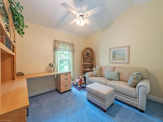 Carpeted home office with lofted ceiling, ceiling fan, and built in desk
