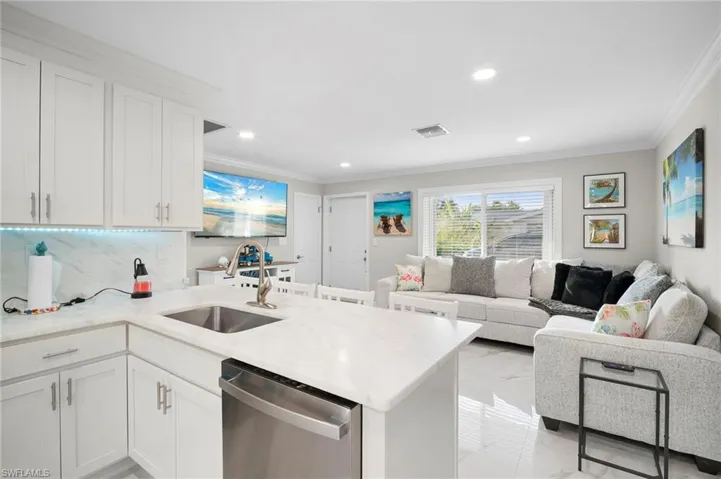 Kitchen featuring stainless steel dishwasher, white cabinetry, light marble finish flooring, open floor plan, and ornamental molding
