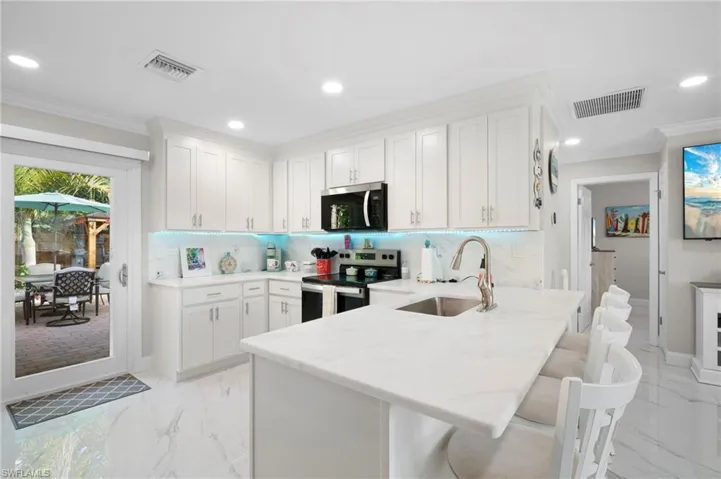Kitchen with crown molding, light marble finish floors, appliances with stainless steel finishes, white cabinetry, and a kitchen breakfast bar
